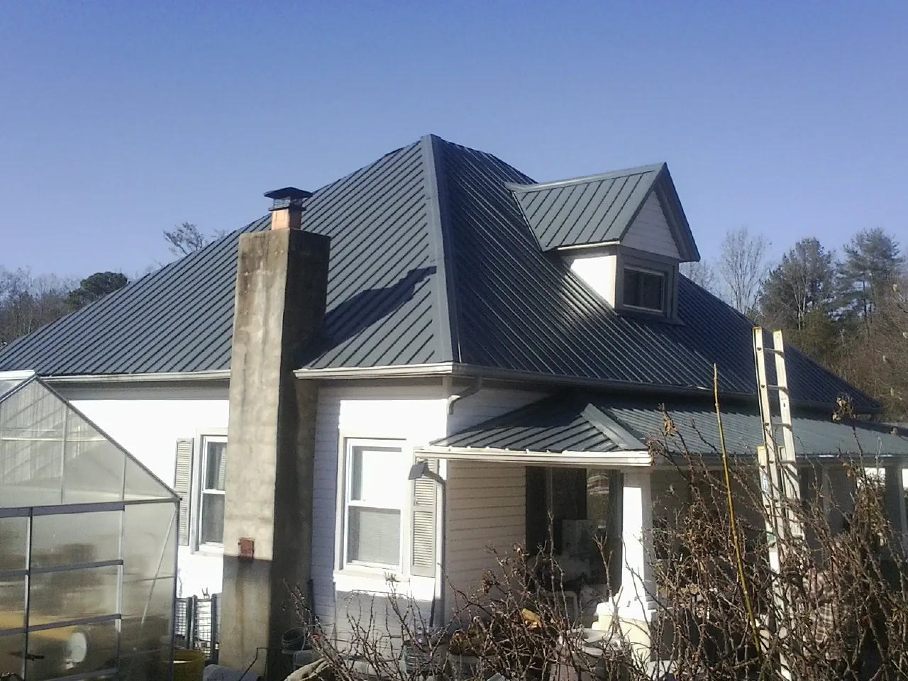 Dark blue standing seam metal roof on a white farmhouse with dormer — Slate & Tile Roof Repair by Roofing Brothers in Dansville