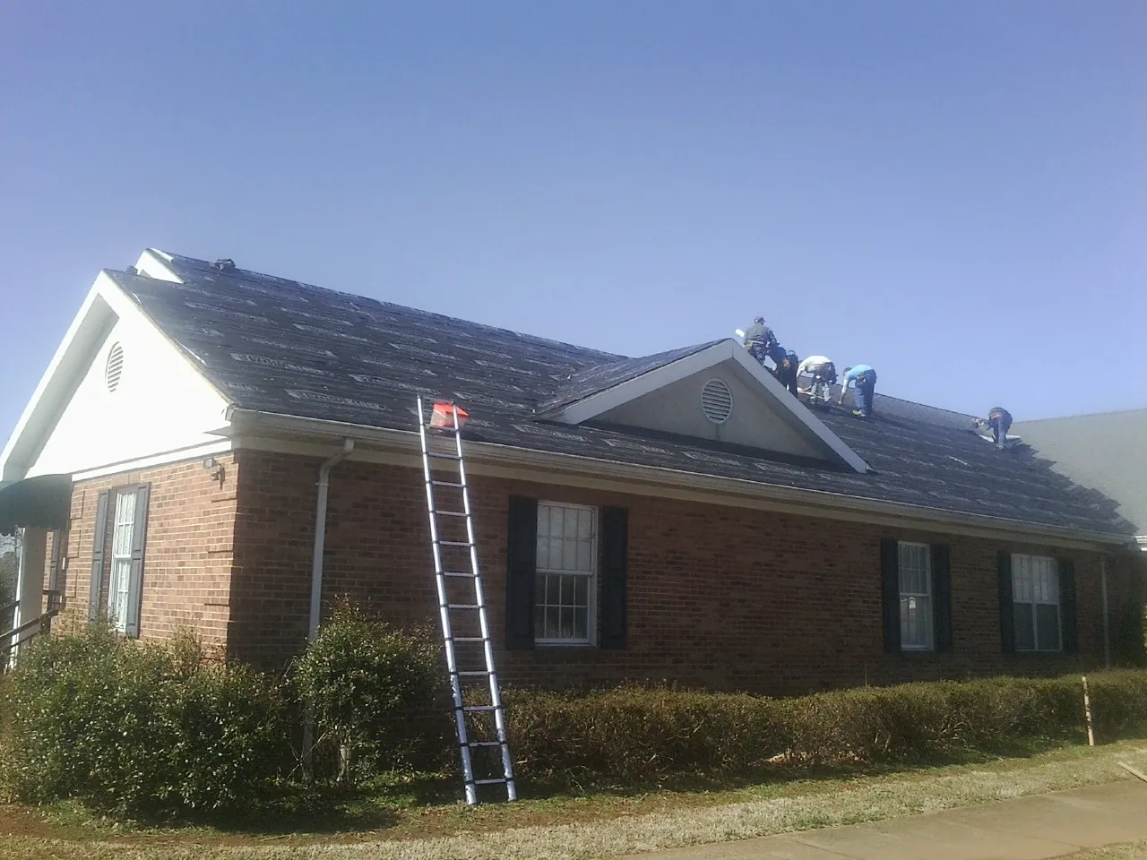 Crew tearing shingles off a brick ranch roof with a ladder set — Metal Roof Repair work by our crew in Dansville