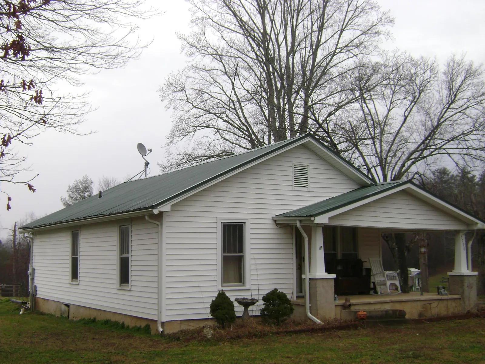 Green metal roof on a white bungalow with a side porch in Dansville