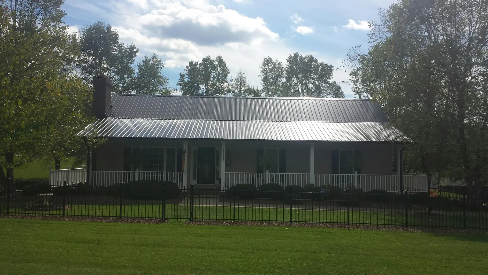 Gray metal roof on a brick ranch with a full width front porch — Gutter Guard Installation work by our crew in Dansville