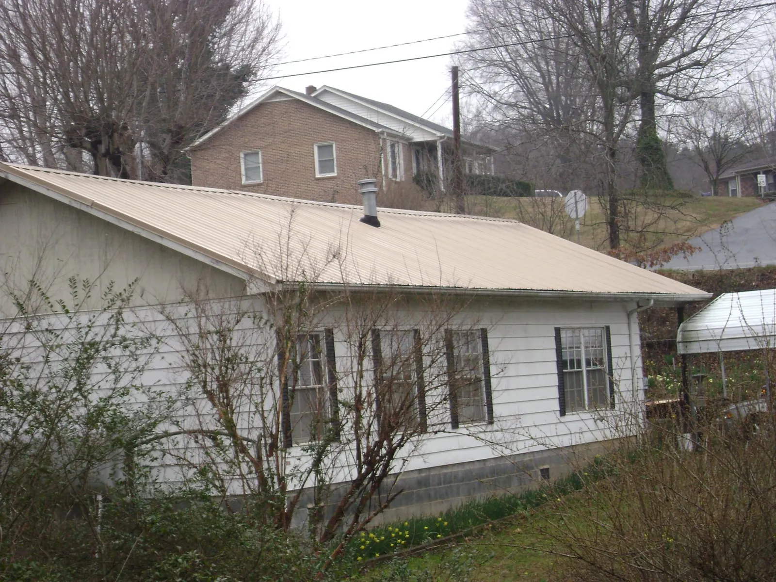 Tan metal roof on a white sided house set into a hillside — Commercial Roofing by Roofing Brothers in Dansville